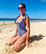 Janni hoenscheid sitzt am strand im blau weiss gestreiften bikini